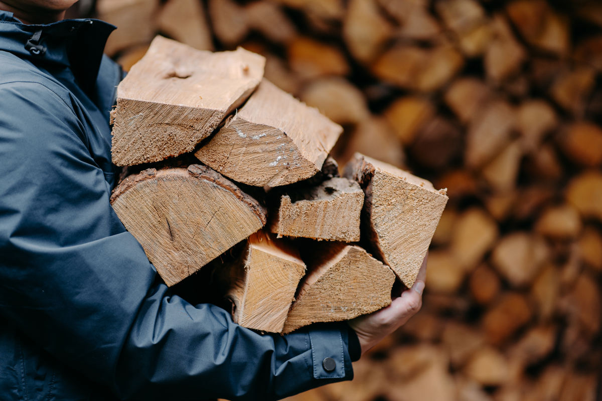 Person trägt Holzscheite fürs Brennholz lagern